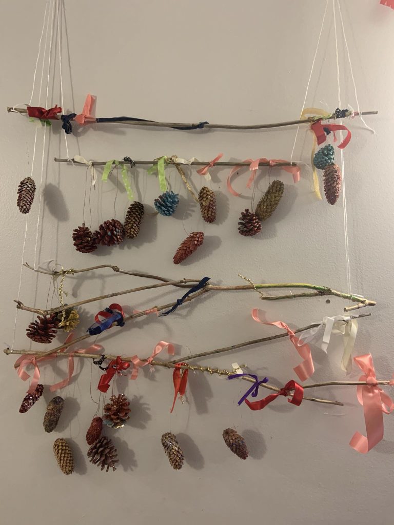 Cocottes de pins colorées accrochées à des branches avec des rubans décoratifs.