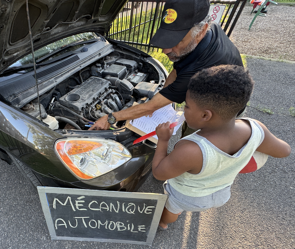 L'animateur de la mécanique auto qui enseigne à un jeune garçon le matériel en devant de la voiture