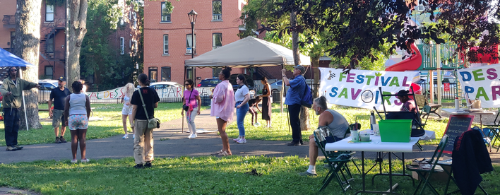 Des gens qui se rassemblent dans le parc avec une banderole qui dit Festival des savoirs partagés